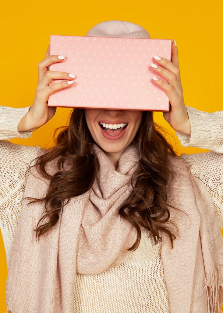 Foto glückliche junge Frau mit einer Geschenkbox in den Händen, die ihr halbes Gesicht mit einem Geschenk bedeckt