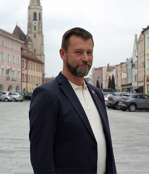 Portrait Foto von Alexander Hauf am Stadtplatz Neuötting mit Kirchturm im Hintergrund.