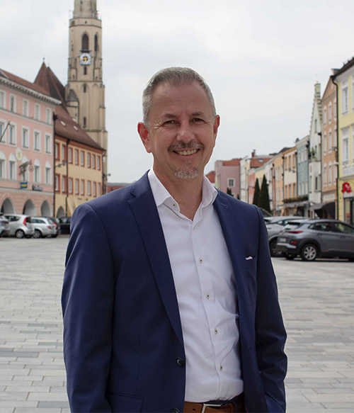Portrait Foto von Engelbert Hascher am Stadtplatz Neuötting mit Kirchturm im Hintergrund.