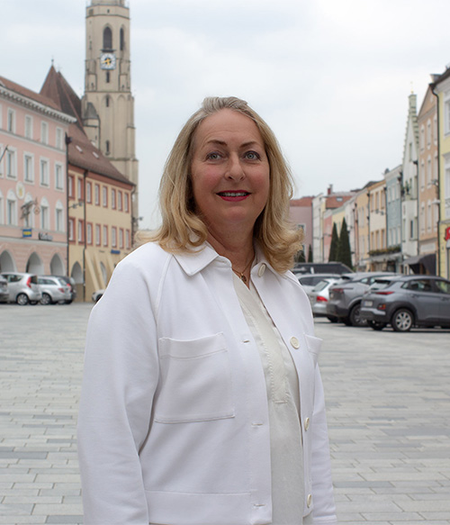 Portrait Foto von Manuela Ganzbeck am Stadtplatz Neuötting mit Kirchturm im Hintergrund.