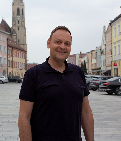 Portrait Foto von Manuela Ganzbeck am Stadtplatz Neuötting mit Kirchturm im Hintergrund.
