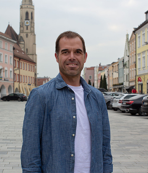 Portrait Foto von Manuela Ganzbeck am Stadtplatz Neuötting mit Kirchturm im Hintergrund.