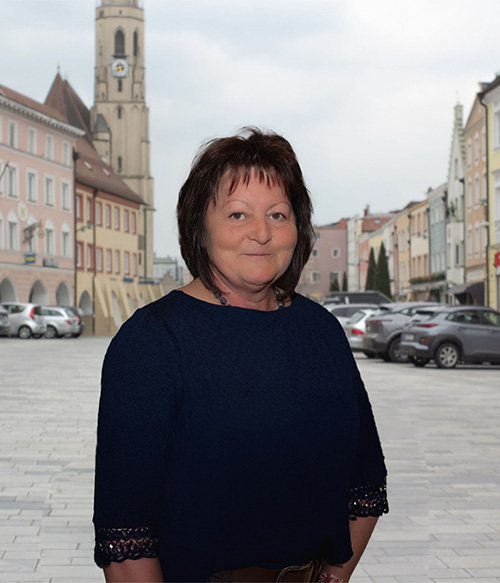 Portrait Foto von Monika Steinlehner am Stadtplatz Neuötting mit Kirchturm im Hintergrund.