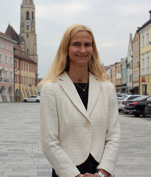 Portrait Foto von Verena Mayer am Stadtplatz Neuötting mit Kirchturm im Hintergrund.